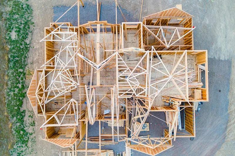 Aerial view of a wood-framed house under construction, roof trusses set across the floor plan