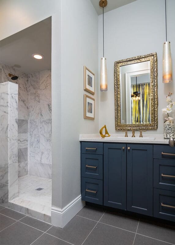 Budget bath with dark blue vanity, gold accent, marble style tiled shower, and pendant light fixtures