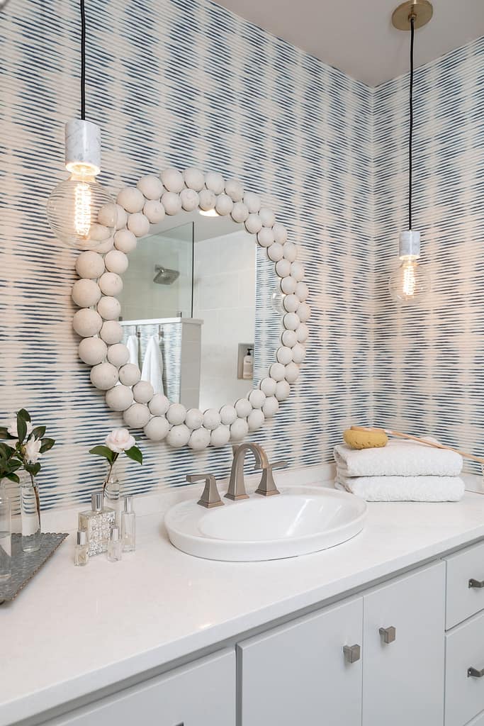 White and Blue Bathroom with wallpaper and white mirror - glass modern pendants - white counter tops with grey cabinets - Scandinavian design