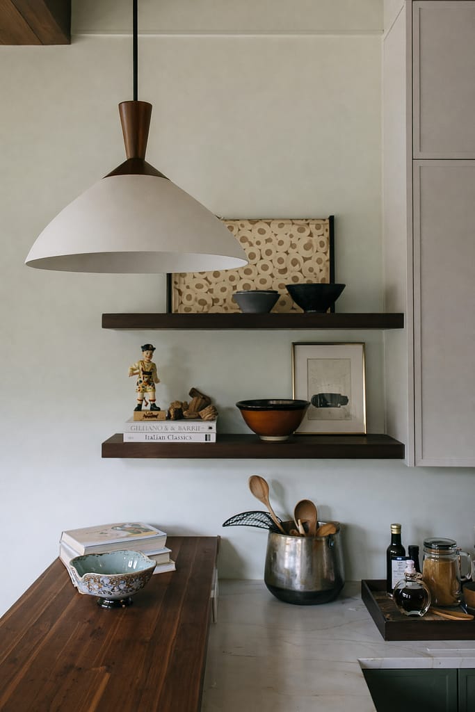 Open kitchen shelving styled with pottery, bowls and a utensil crock beneath a white dome pendant light