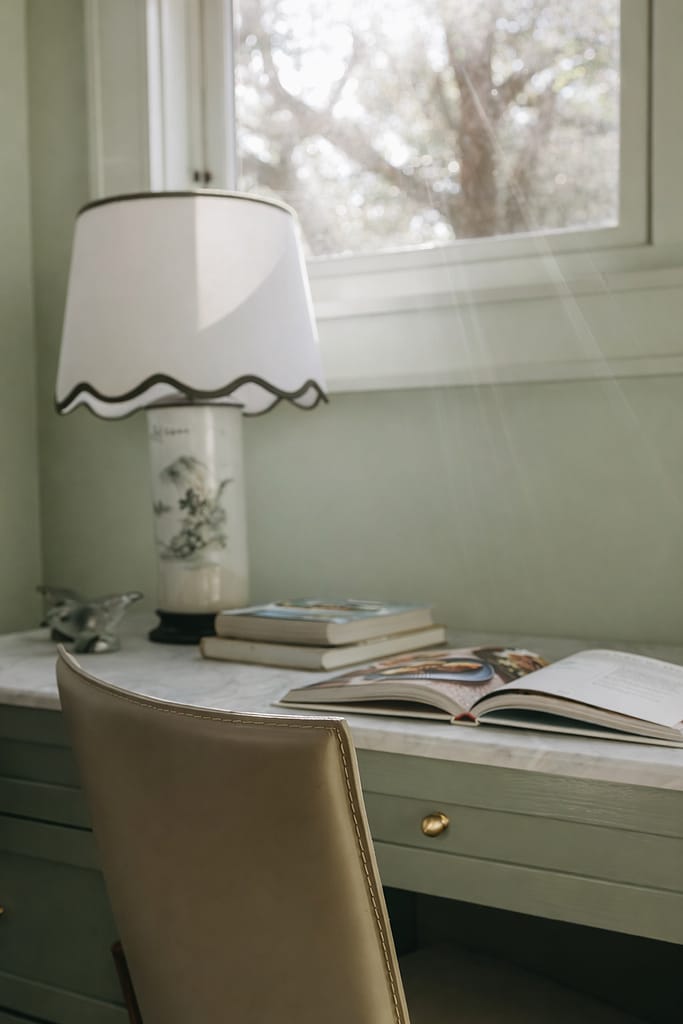 Scalloped white range hood against a sage green wall, with an open book and lamp on the counter below