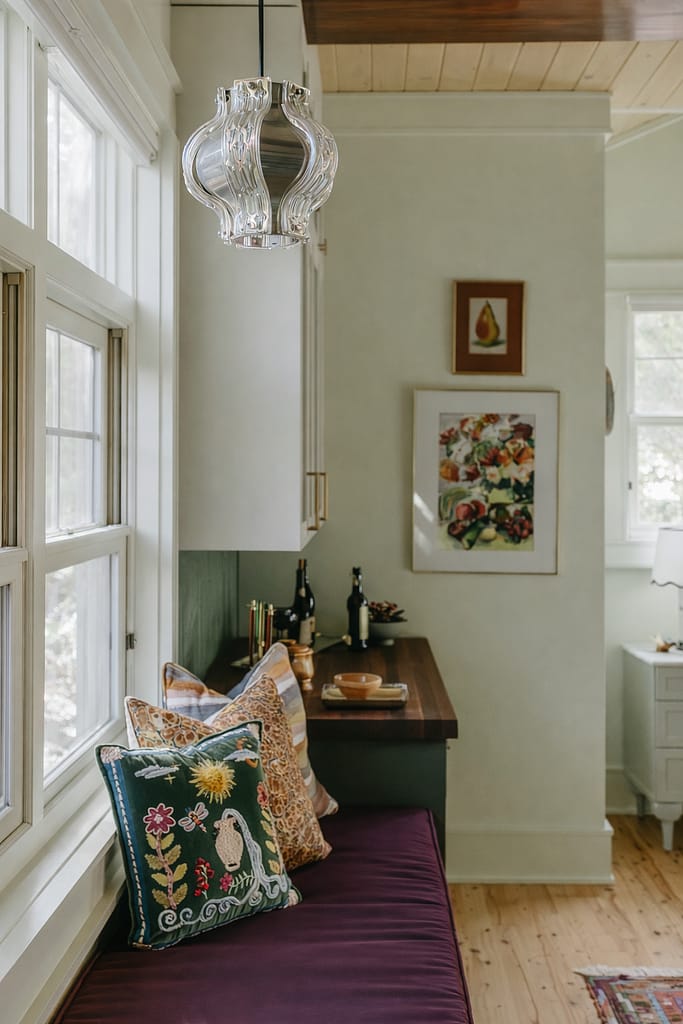 Kitchen corner with floral artwork, patterned cushions on a purple bench seat and bottles on the counter