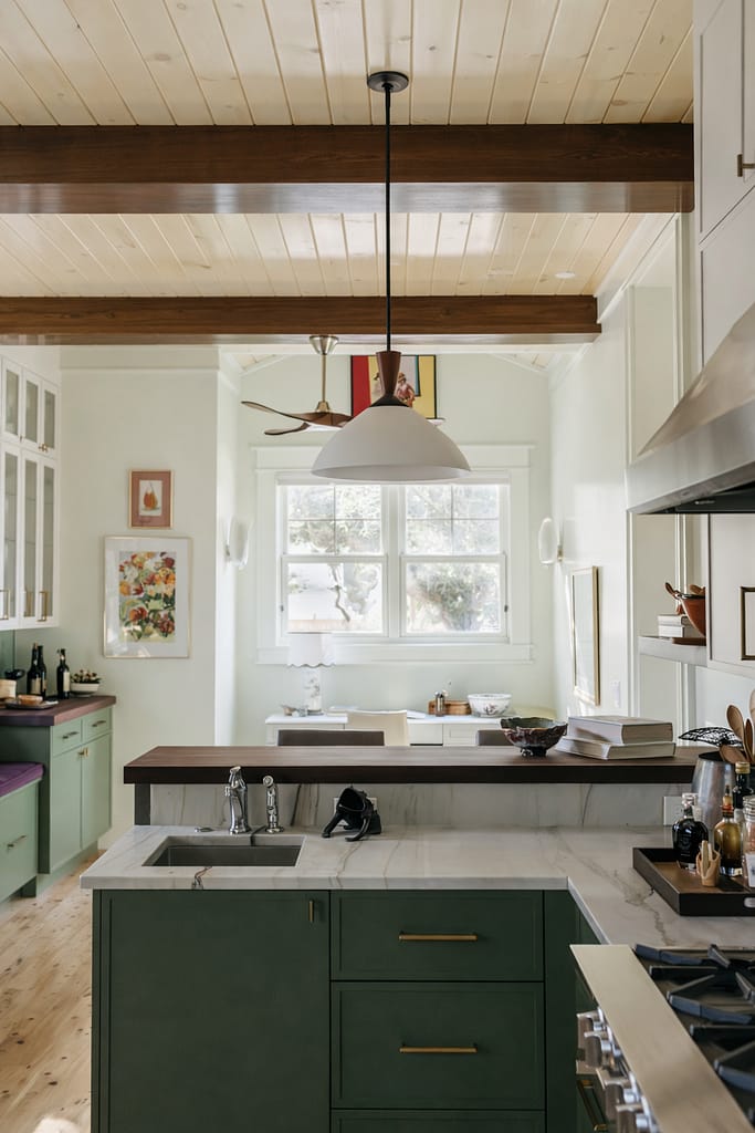 Eclectic kitchen with sage green lower cabinets, white uppers, exposed wood beam and a red pendant light over a marble island